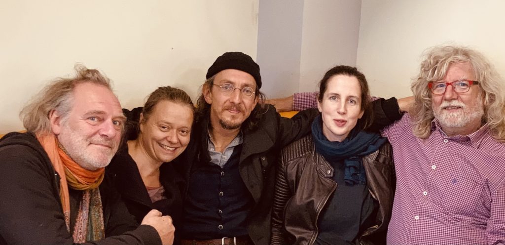 Anna und die Wise Old Men und die zwei beiden Silas und Maria sitzen am Tisch und lachen in die Kamera.